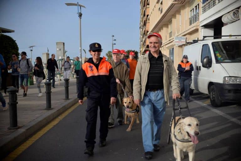 Un agente de policía local acompaña a un hombre con su perro guía labrador claro.